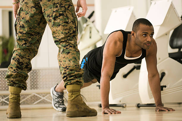 Bootcamp fitness trainer standing over trainee as he does Burpees a full body workout exercise. Horizontal shot.