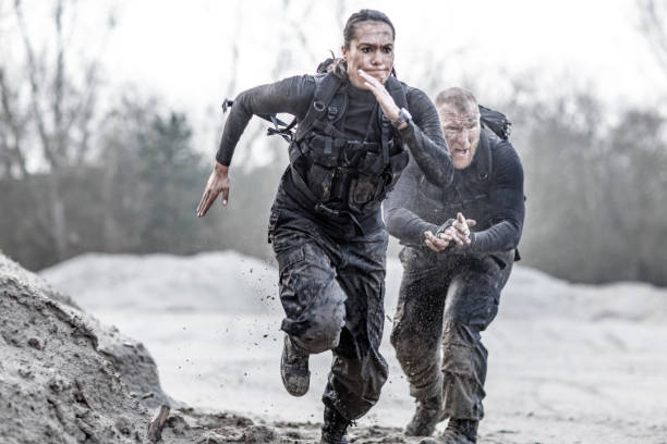 Redhead male drill instructor training beautiful brunette female soldier doing sprints outdoors in the mud